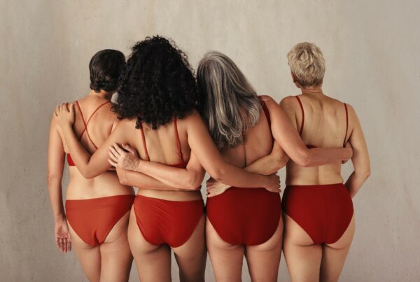Four women in red undergarments facing the back with their arms around each other